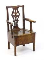 A late Georgian oak commode chair with a Chippendale style back splat above a hinged seat opening to