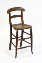 A Victorian child's chair with a bowed top and mid rail above a caned seat and raised on turned