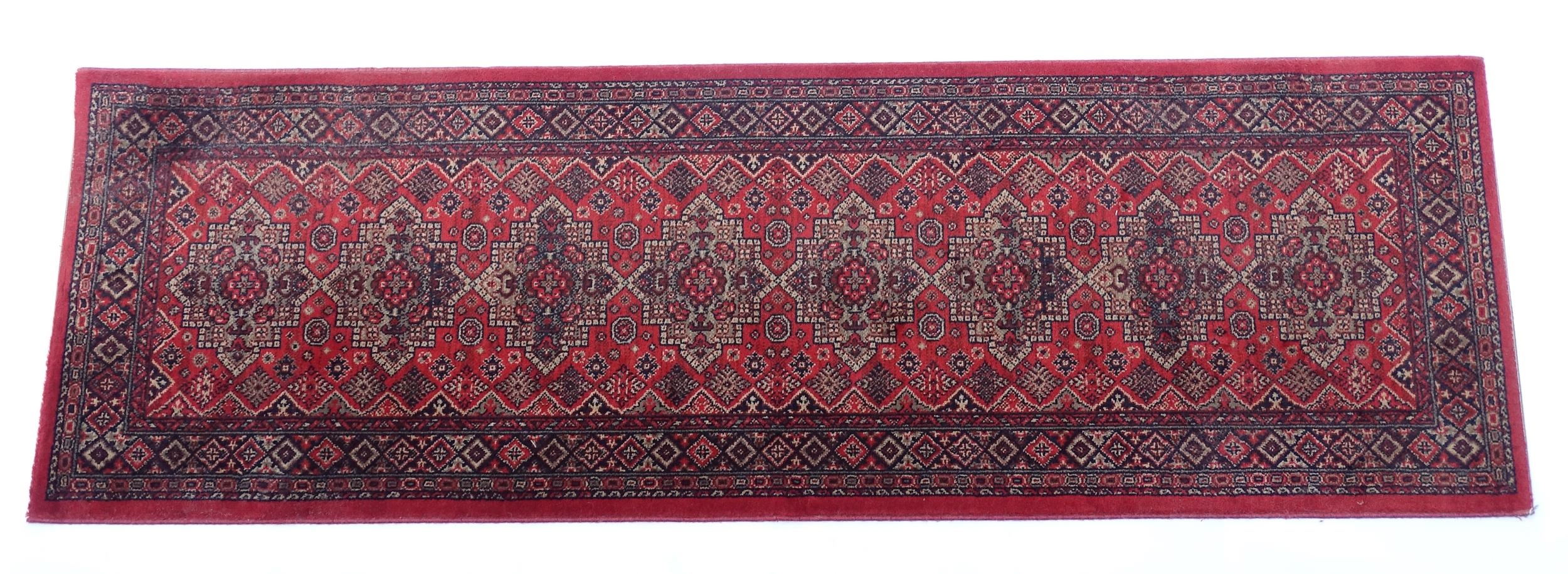 Carpet / Rug : A red ground runner with repeating motifs to centre, bordered by geometric banding.