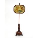 A mid 19thC mahogany pole screen, with a glazed adjustable screen having a needlework centre and