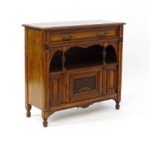 An Aesthetic movement walnut side cabinet with a chamfered frame and carved floral decoration, the