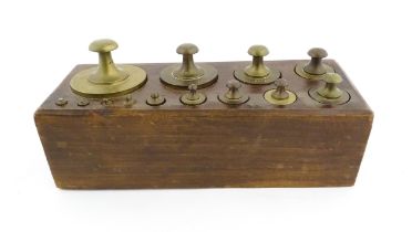 A 20thC set of 13 brass graduated weights from 2g to 2kg within a wooden block. Approx. 10 1/2" wide