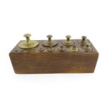 A 20thC set of 13 brass graduated weights from 2g to 2kg within a wooden block. Approx. 10 1/2" wide