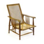 An Arts & Crafts bergère chair with a caned backrest and seat, the shaped arms supported by turned