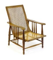An Arts & Crafts bergère chair with a caned backrest and seat, the shaped arms supported by turned