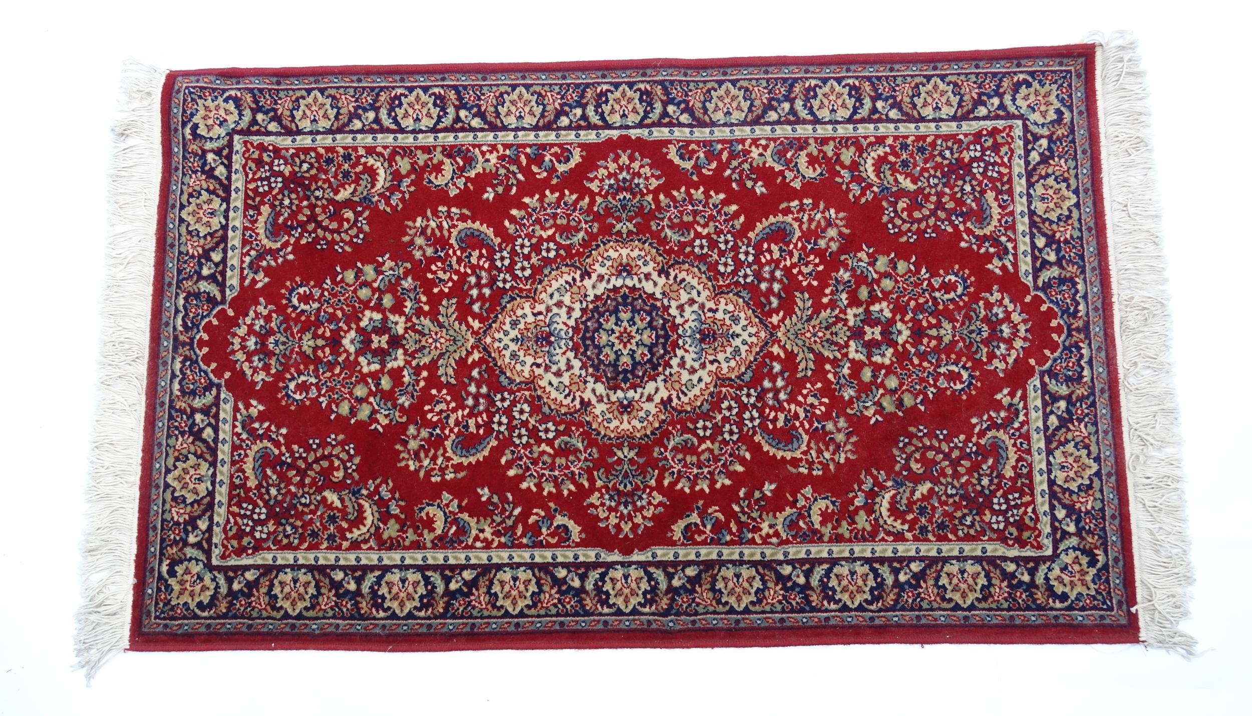 Carpet / Rug : A red ground rug with central cream and blue vignette, decorated with floral and