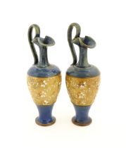 A pair of Royal Doulton stoneware jugs of Classical ewer form with floral and foliate decoration.