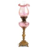 Ornate gilt painted oil lamp with iridescent cranberry glass shade and reservoir, 68.5cm high :