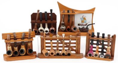 Twenty three vintage tobacco smoking pipes arranged in five pipe racks, two in the form of a gate,