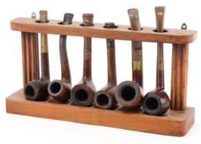 Six vintage Orlik Deluxe tobacco smoking pipes arranged in a lightwood pipe rack, the rack 28cm wide