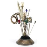 Silver hatpin stand housing various hatpins including simulated pearl and sequinned examples, the