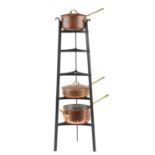 Three Victorian coppered and brass saucepans housed in a tapering wrought cast iron rack : For