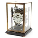 Champleve enamel rolling ball clock housed in a glazed brass case on hardwood stand, the circular