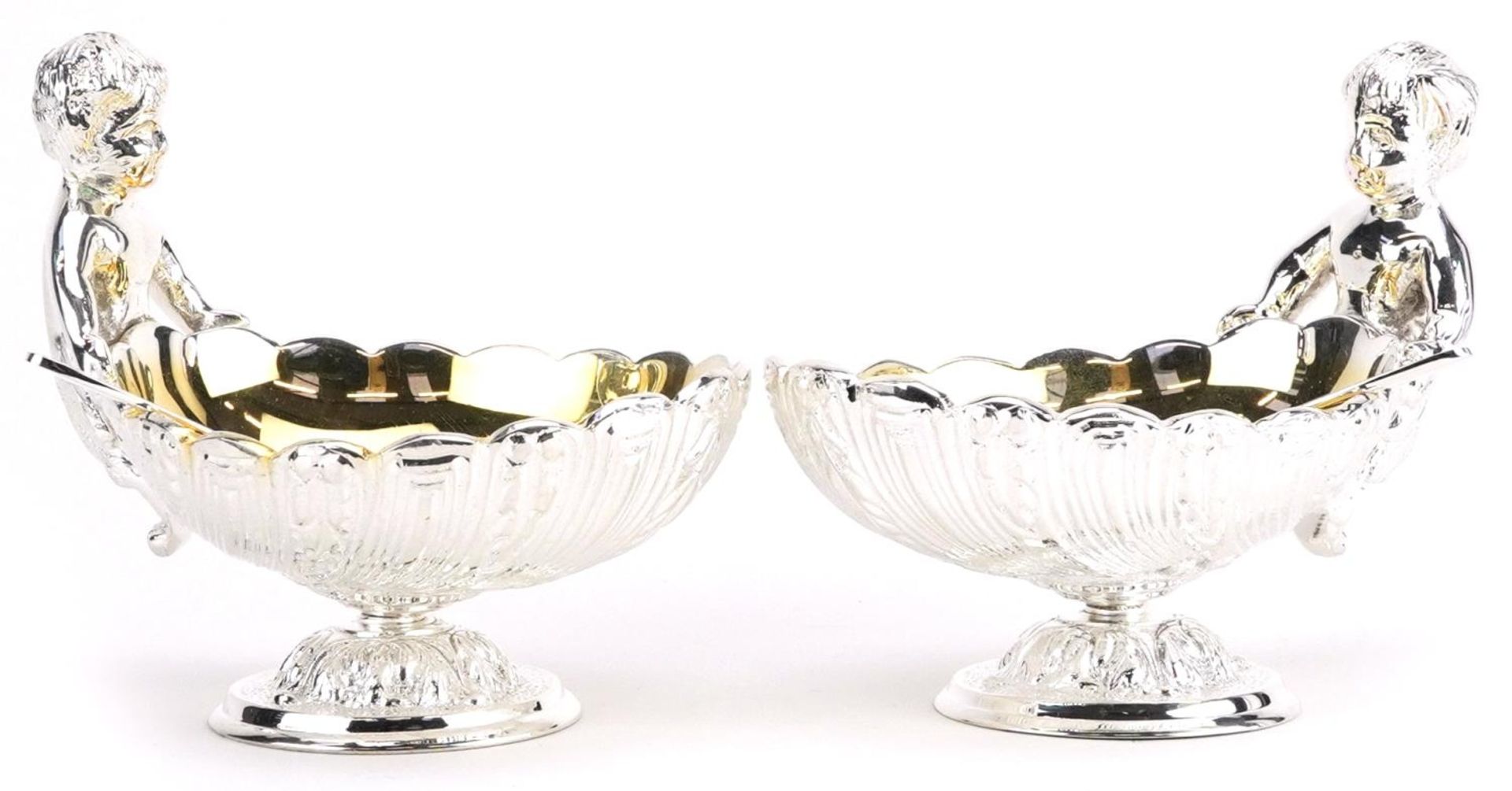Pair of silver plated open table salts with spoons in the form of Putti holding a shell, 12cm in