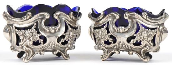 William Oliver, pair of Art Nouveau pierced and embossed silver open salts with blue glass liners,