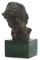 Patinated bronze head and shoulders bust of a young female wearing a hat raised on a green marble