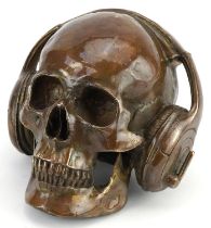 Steam punk interest patinated bronze model of a human skull wearing headphones, 20cm in length