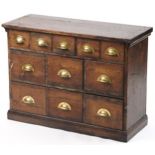 Stained pine haberdashery chest fitted with an arrangement of eleven drawers having brass handles,