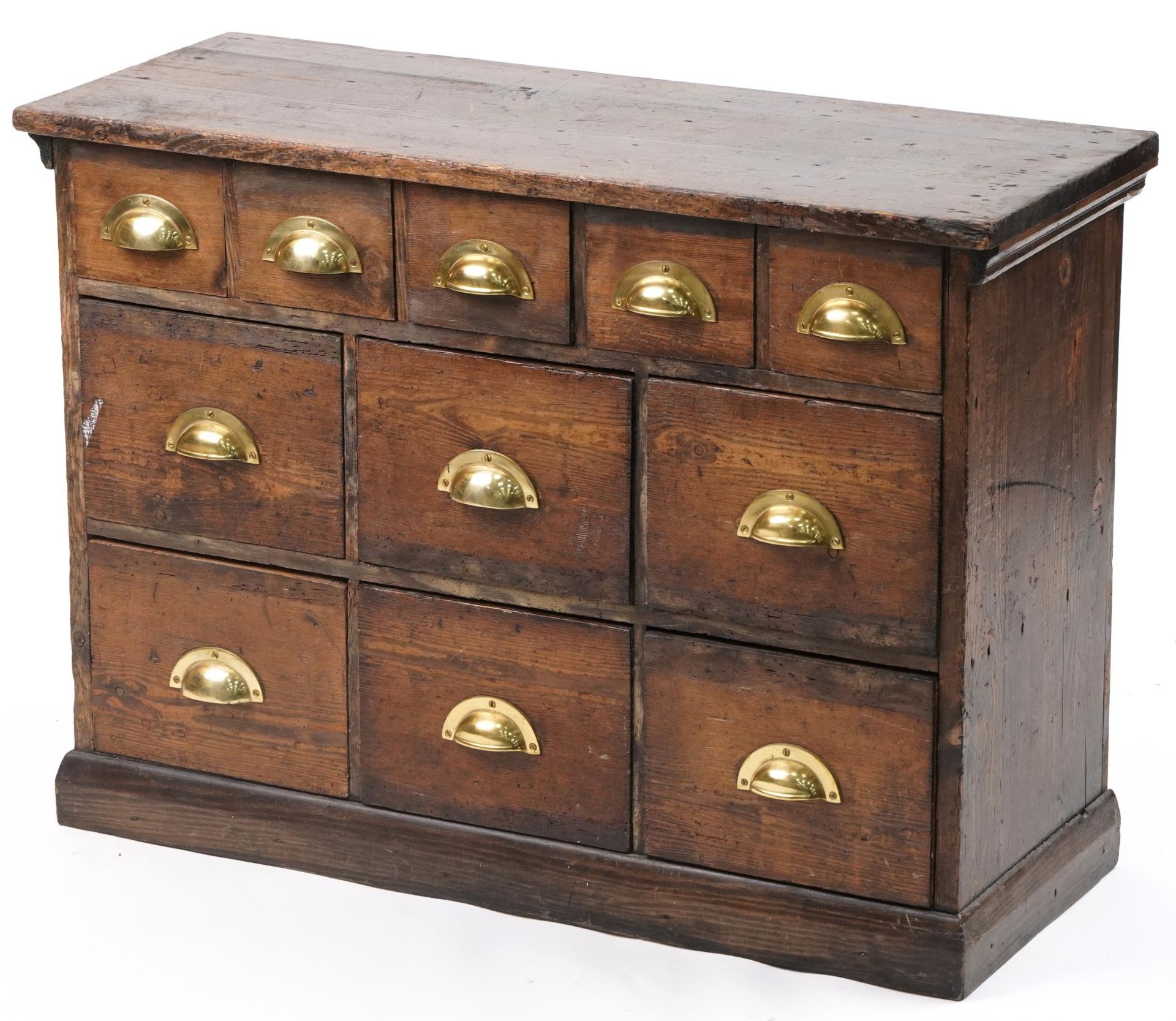 Stained pine haberdashery chest fitted with an arrangement of eleven drawers having brass handles,
