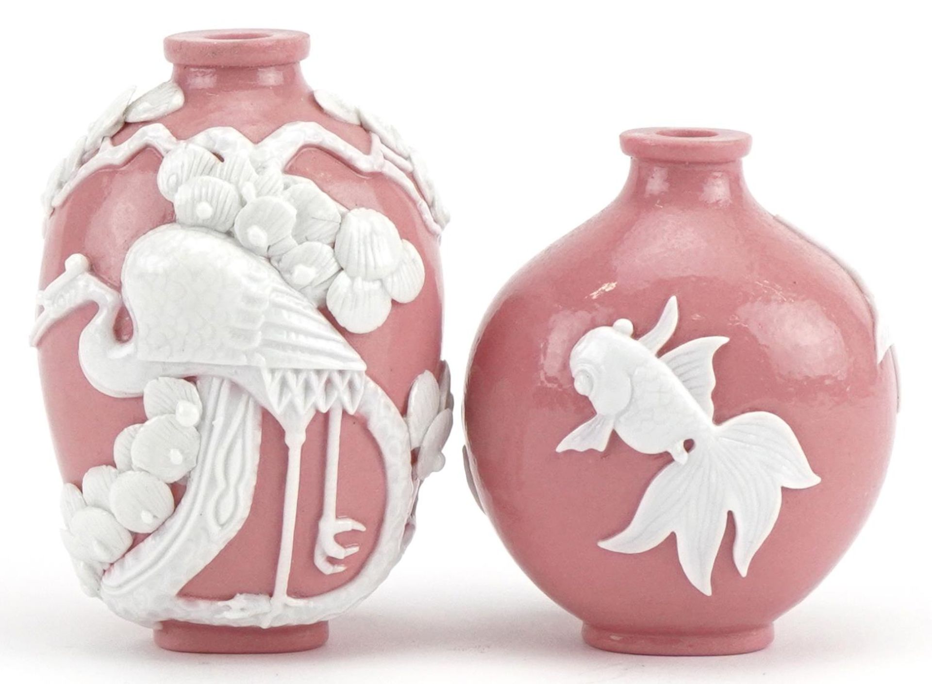 Two Chinese porcelain pink ground snuff bottles decorated in relief with fish and a crane, the