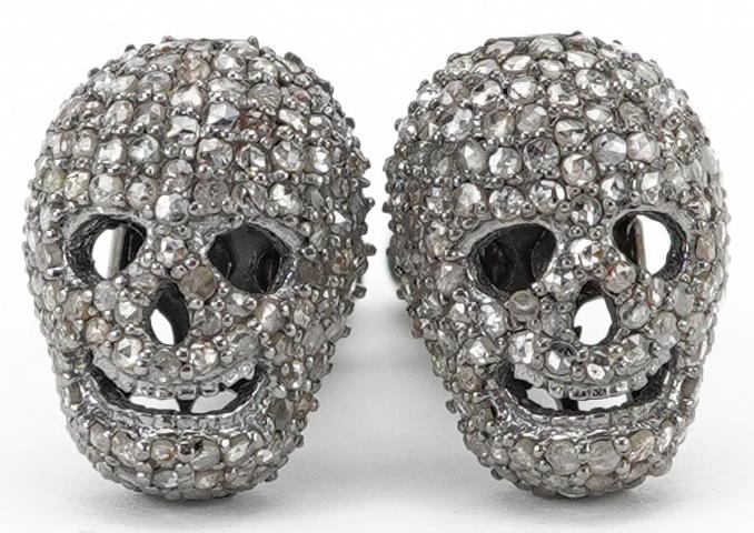 Pair of diamond set white metal cufflinks in the form of human skulls, total diamond weight