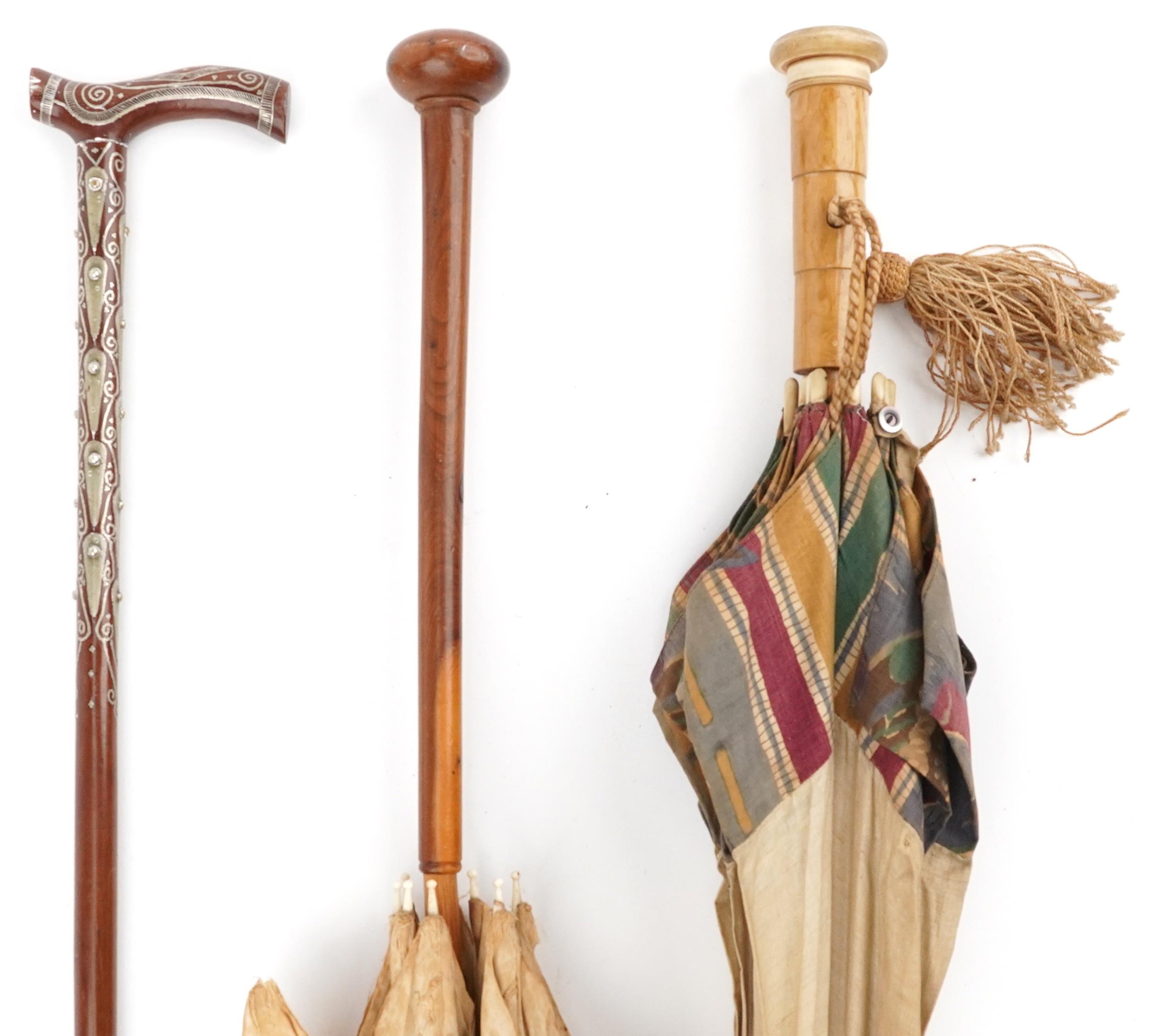 Two early 20th century parasols and a Middle Eastern hardwood walking stick with foliate metal