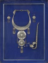 Thai white metal jewellery and opium pipe housed in a glazed framed display, overall 55cm x 42.5cm