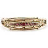 Edwardian 9ct rose gold hinged bangle set with eleven graduated red stones and seed pearls,