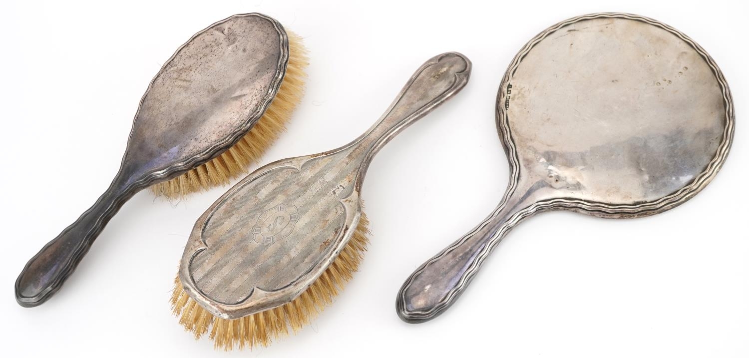 Two Edwardian silver backed clothes brushes and a hand mirror, the largest 27cm in length