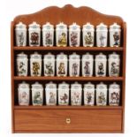 Collection of M J Hummel porcelain spice jars and covers arranged in a lightwood spice rack, each