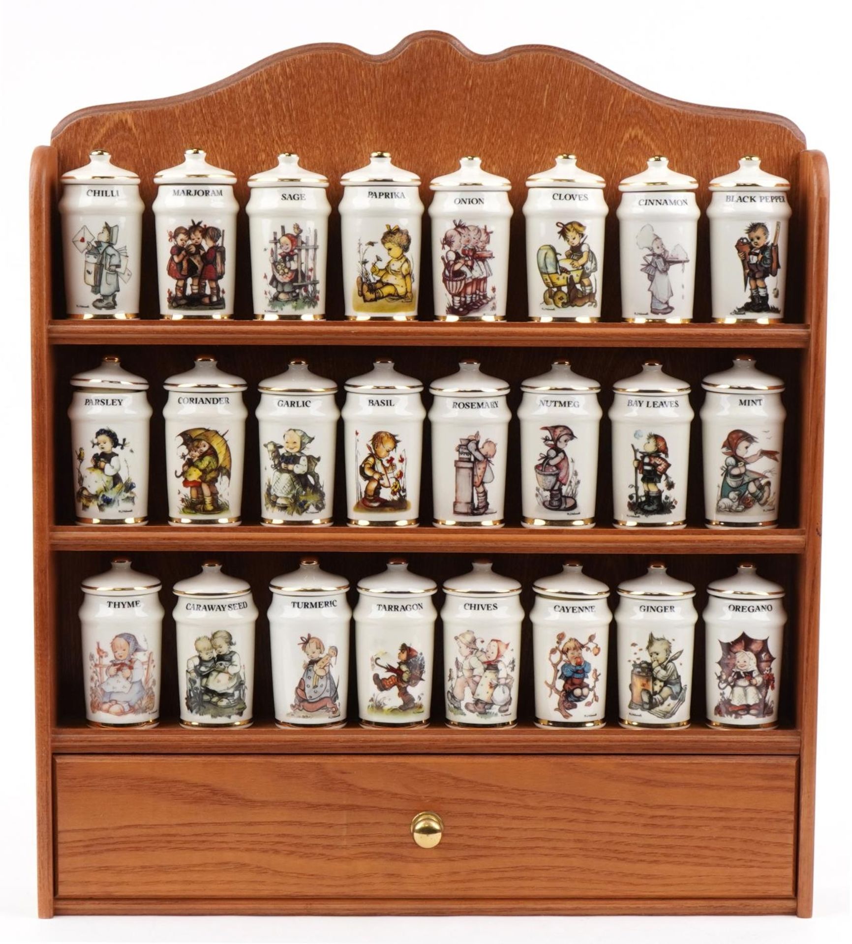 Collection of M J Hummel porcelain spice jars and covers arranged in a lightwood spice rack, each