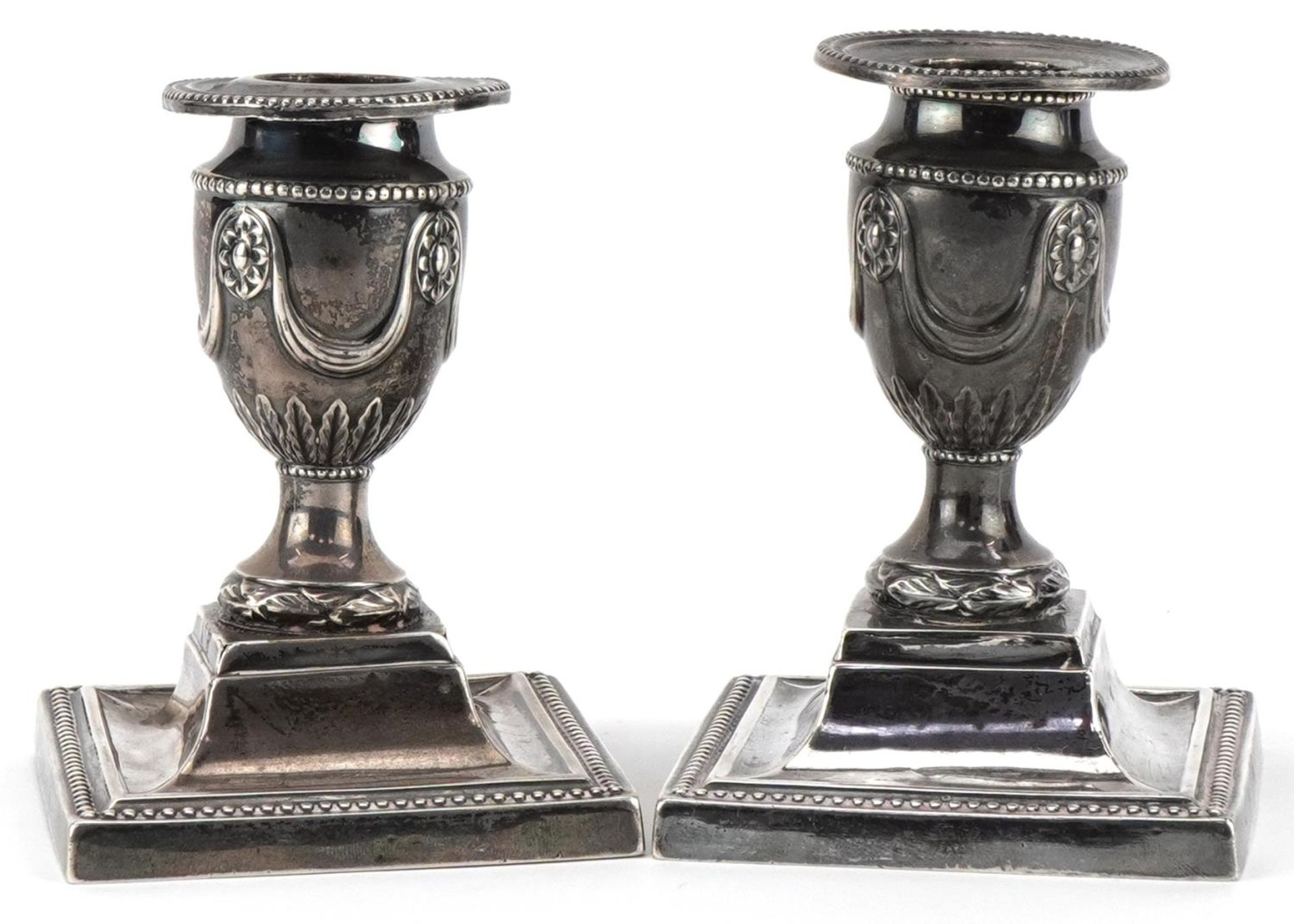 James Dixon & Sons, pair of Edwardian silver campana urn dwarf candlesticks embossed with flowers