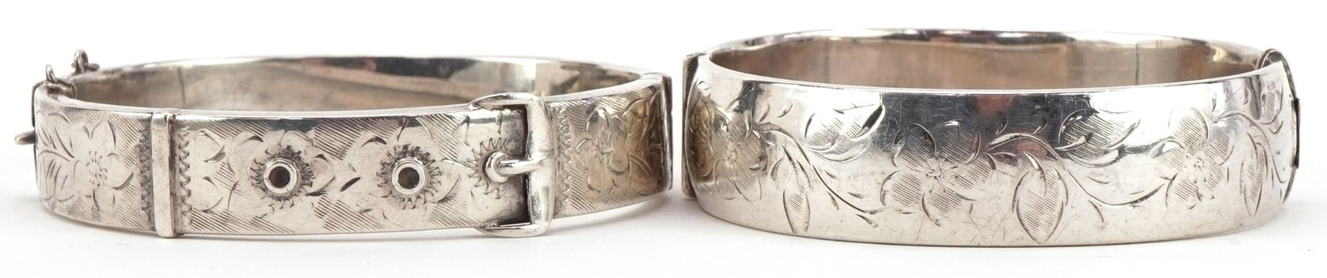 Two Victorian style floral engraved hinged bangles, one in the form of a buckle, each 6.5cm wide,