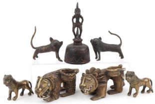 Six African Benin bronzed mythical lions and a figural table bell, the largest 13.5cm high