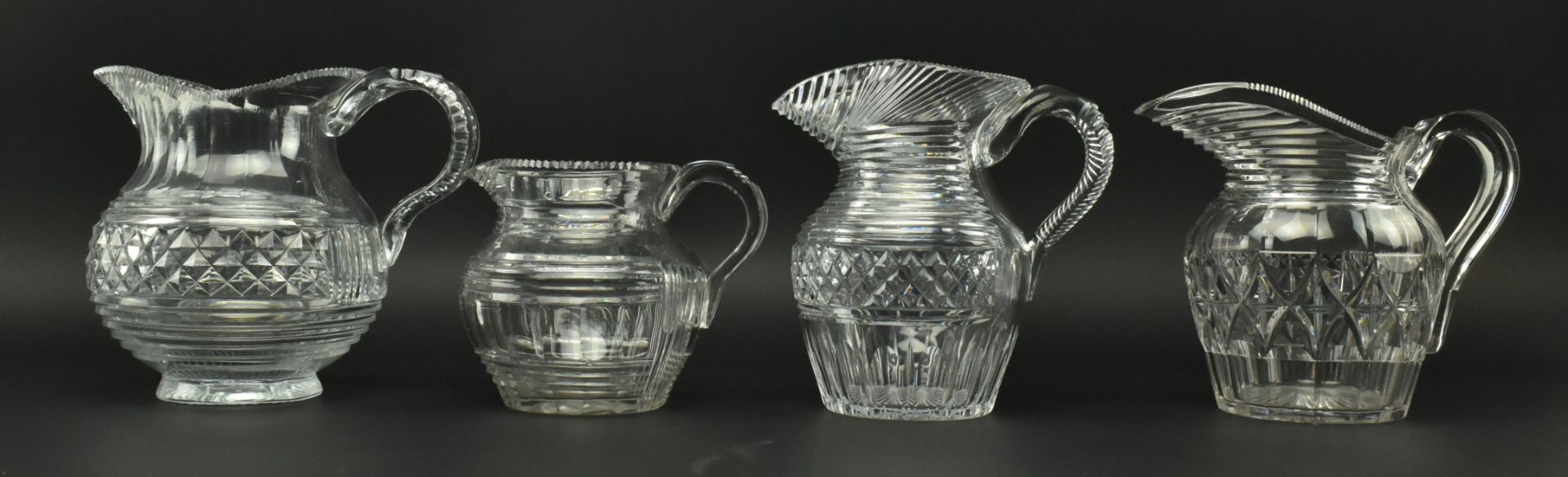 FOUR EARLY 19TH CENTURY GLASS JUGS WITH STEP CUT DESIGN