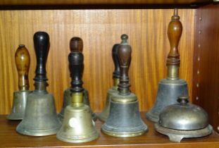 A collection of seven brass hand bells with turned wood handles and a reception bell by Russell