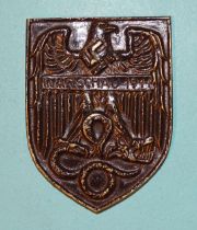 A cast metal example of the Warsaw Shield, 7.2 x 5.4cm.