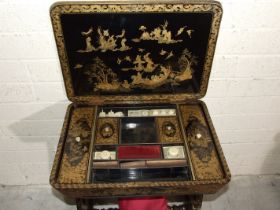 A Victorian lacquered work table with fitted interior and pull-out work bag, on end supports and