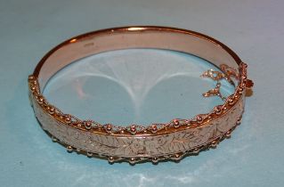 A 9ct rose gold hinged bangle with engraved decoration within cannetile border, internal