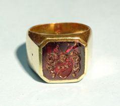 An unmarked gold signet ring set square intaglio carved with a coat of arms, (cracked), tested as