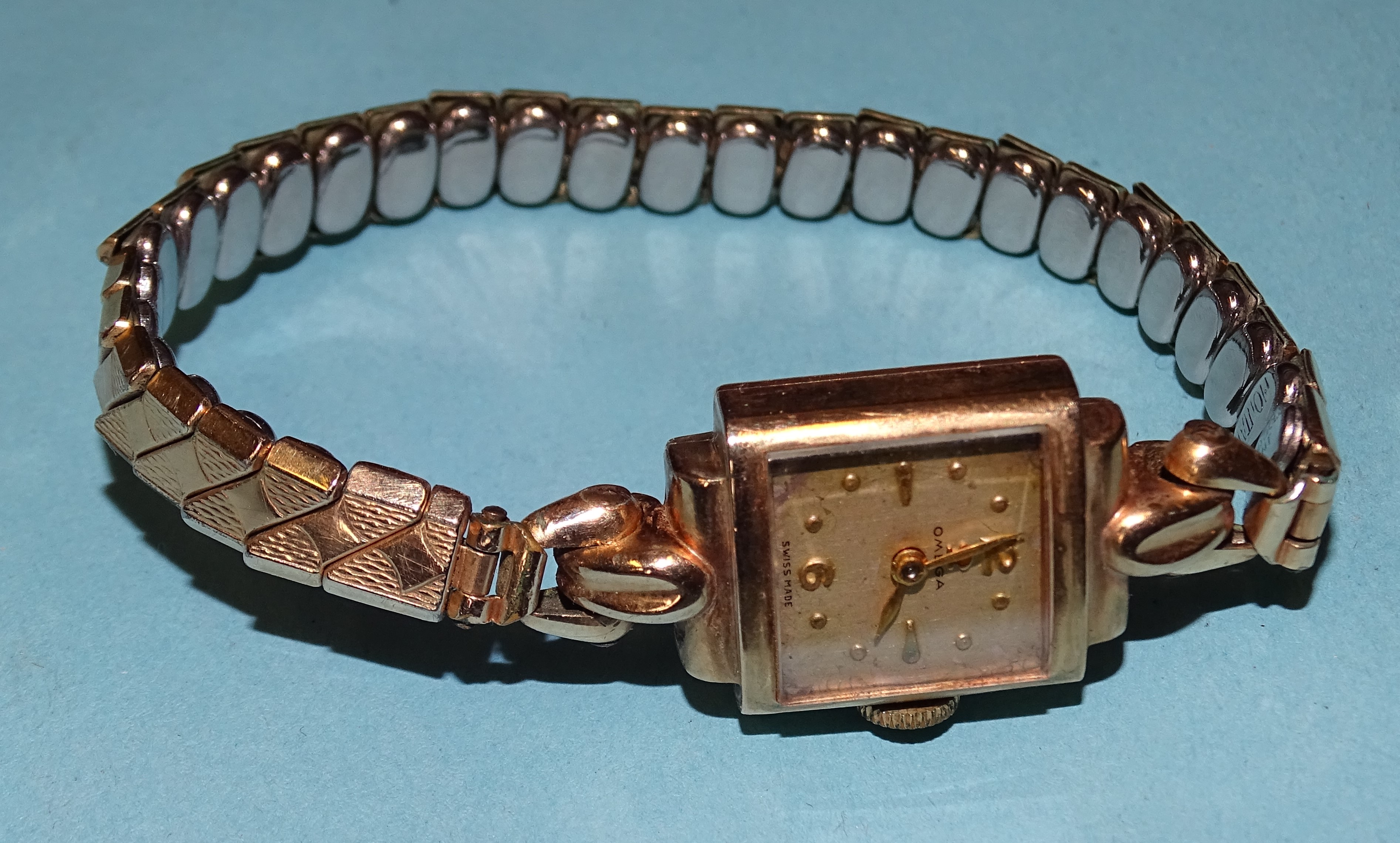 Omega, a lady's 9ct-gold-cased square-faced wrist watch on gold-plated expanding bracelet, with