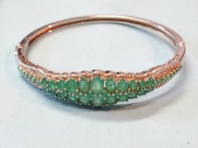 An emerald and silver hinged bangle claw set two rows of graduated oval emeralds with round cuts