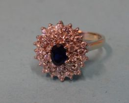 A sapphire and diamond cluster ring claw-set an oval sapphire within two tiers of a total of