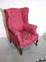 A Georgian-style upholstered wing armchair with shaped wings and serpentine seat, on stained wood