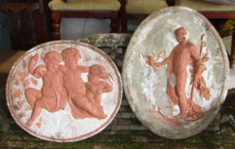 Two cast concrete oval wall plaques decorated with classical figures and putti, 80cm high x 66cm