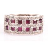 A ruby and diamond band ring, set with twelve square cut rubies, each surrounded by round brilliant