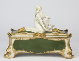 An Art Nouveau biscuit porcelain box, green painted and gilt, the lid with a handle in the form of
