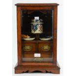 An early 20th century oak smokers cabinet with glazed door, enclosing a fitted interior,