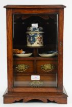 An early 20th century oak smokers cabinet with glazed door, enclosing a fitted interior,