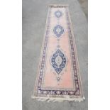 A Turkish pink ground runner, decorated with three blue lozenge within a stylised leaf border,